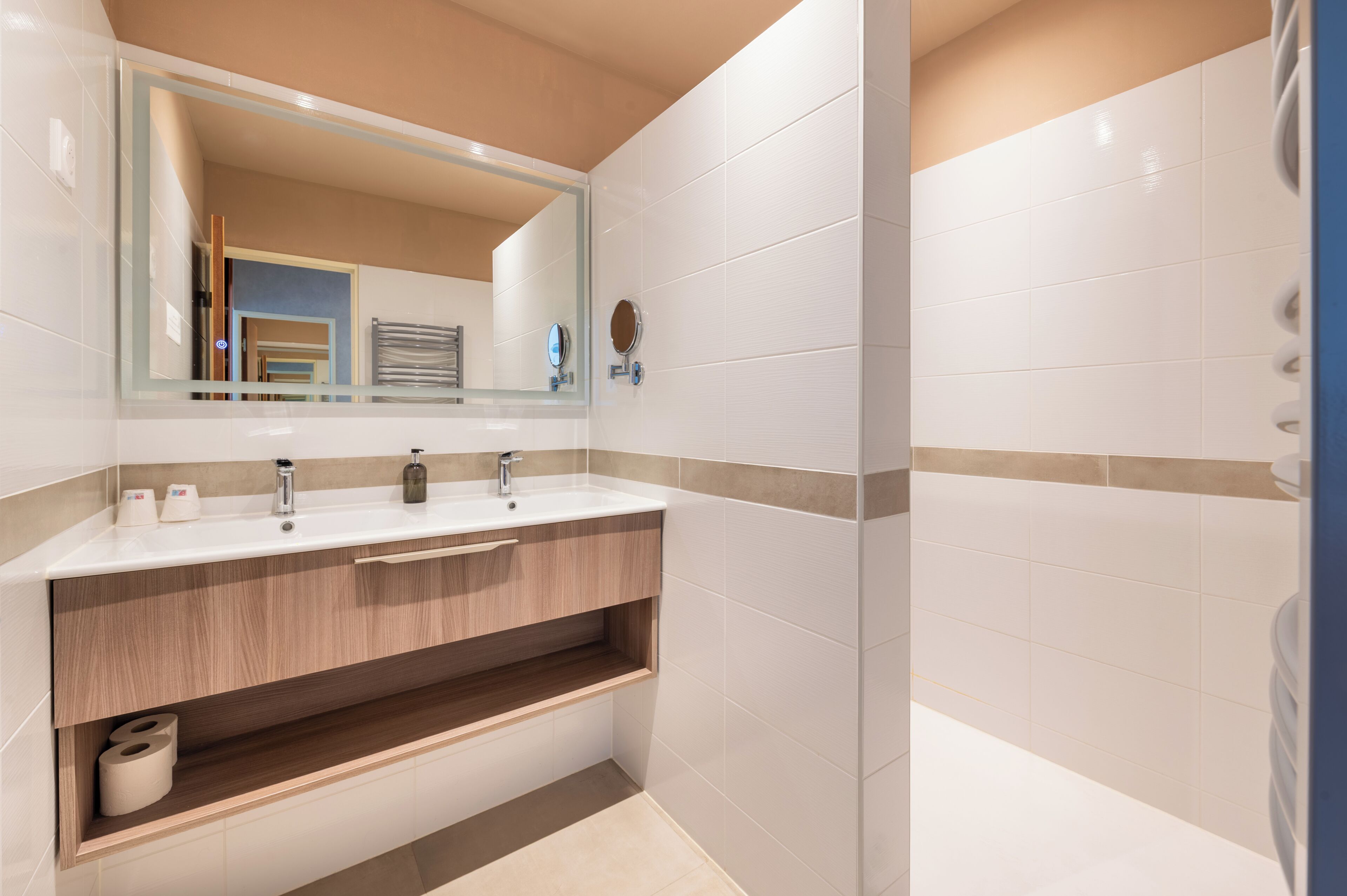 A modern bathroom with a large mirror, two sinks, a vanity with storage, and a shower area.