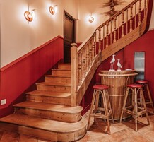 Uma escada de madeira com paredes vermelhas e uma área de bar circular com bancos.