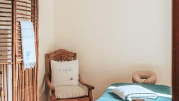 Une pièce chaleureuse avec une chaise en bois, un lit recouvert d'une couverture bleue, un panier en osier contenant du thé et une théière, et un luminaire suspendu en fibres tressées.