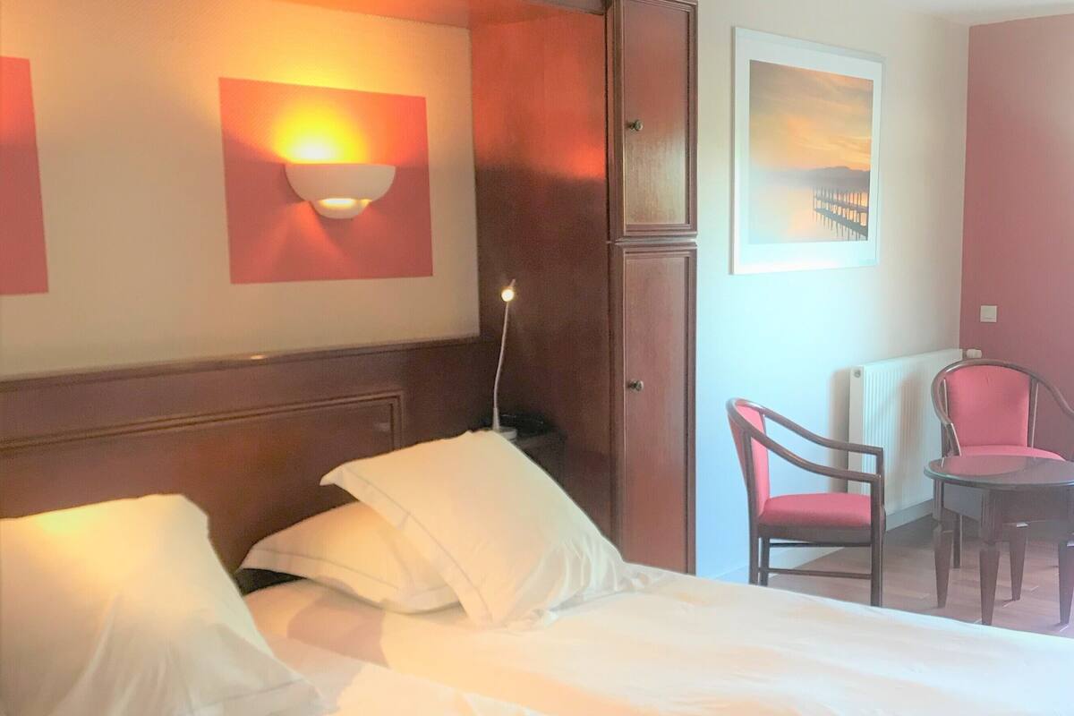 A hotel room with a large bed, a wooden headboard, a desk with a chair, and a wall-mounted light fixture.