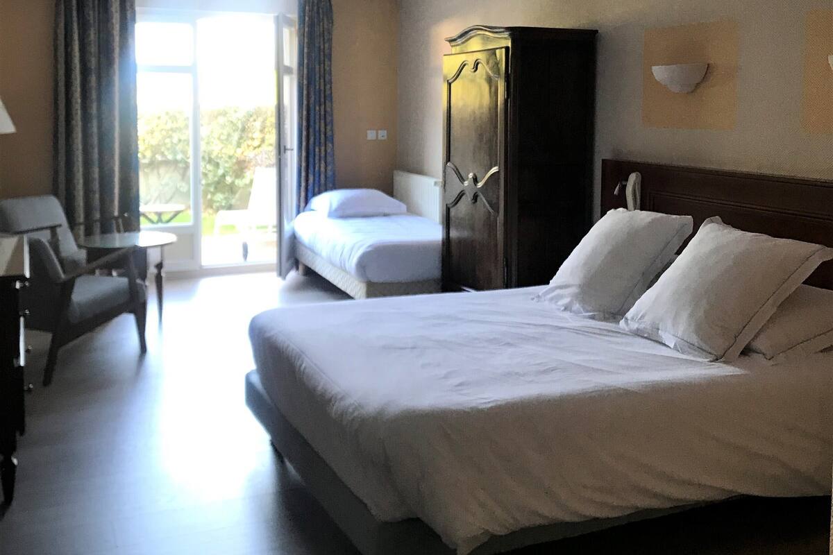 A hotel room with a large bed, a desk, a chair, a wardrobe, and a view of the outdoors.