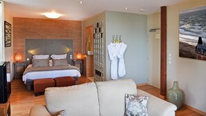 A modern hotel room with a large bed, a sitting area with a sofa, a mirror, and a painting of the ocean. - Hotel Restaurant Le Bellevue (Villerville)