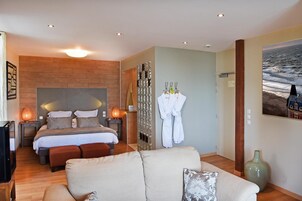 Quarto de hotel moderno com uma cama grande, área de estar com sofá, espelho e pintura do oceano.