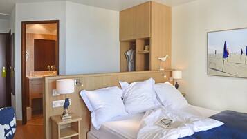 Habitación de hotel con cama, lámparas de noche, armario de madera, espejo y un cuadro con motivos playeros.