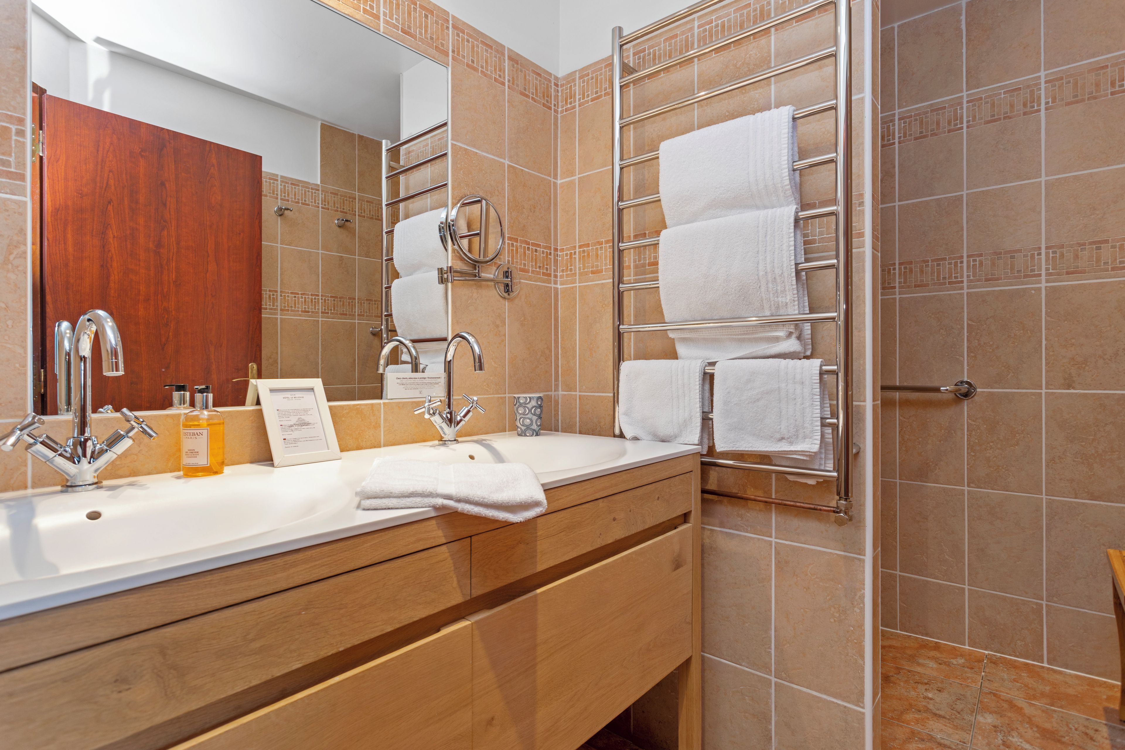 Une salle de bain avec un lavabo double, deux robinets, un miroir, un porte-serviettes et un flacon de savon.