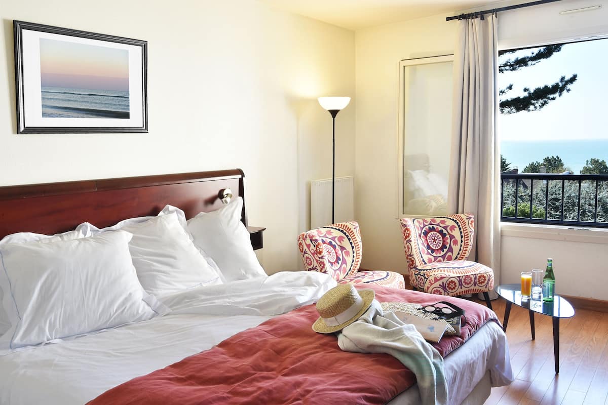 A hotel room with a bed, a chair, a table with drinks, and a view of the sea.