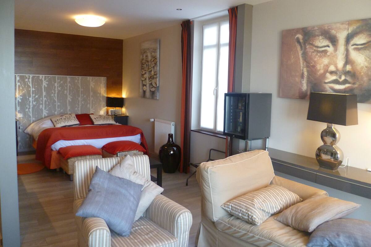 A hotel room with a bed, two armchairs, a TV, and artwork on the walls.