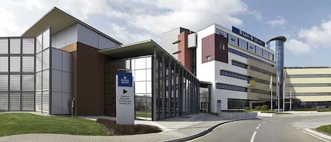 Een modern gebouw met een receptie, parkeerplaats en een bord met de tekst RMH Des Arts.