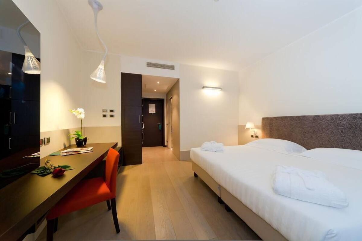 Habitación de hotel con cama, escritorio, silla, televisor y planta en maceta.