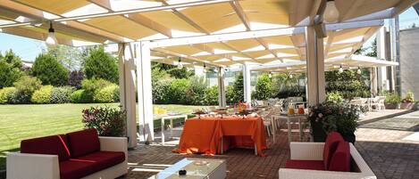 Un patio al aire libre con mobiliario de mimbre, una mesa con mantel naranja y vistas a un jardín.