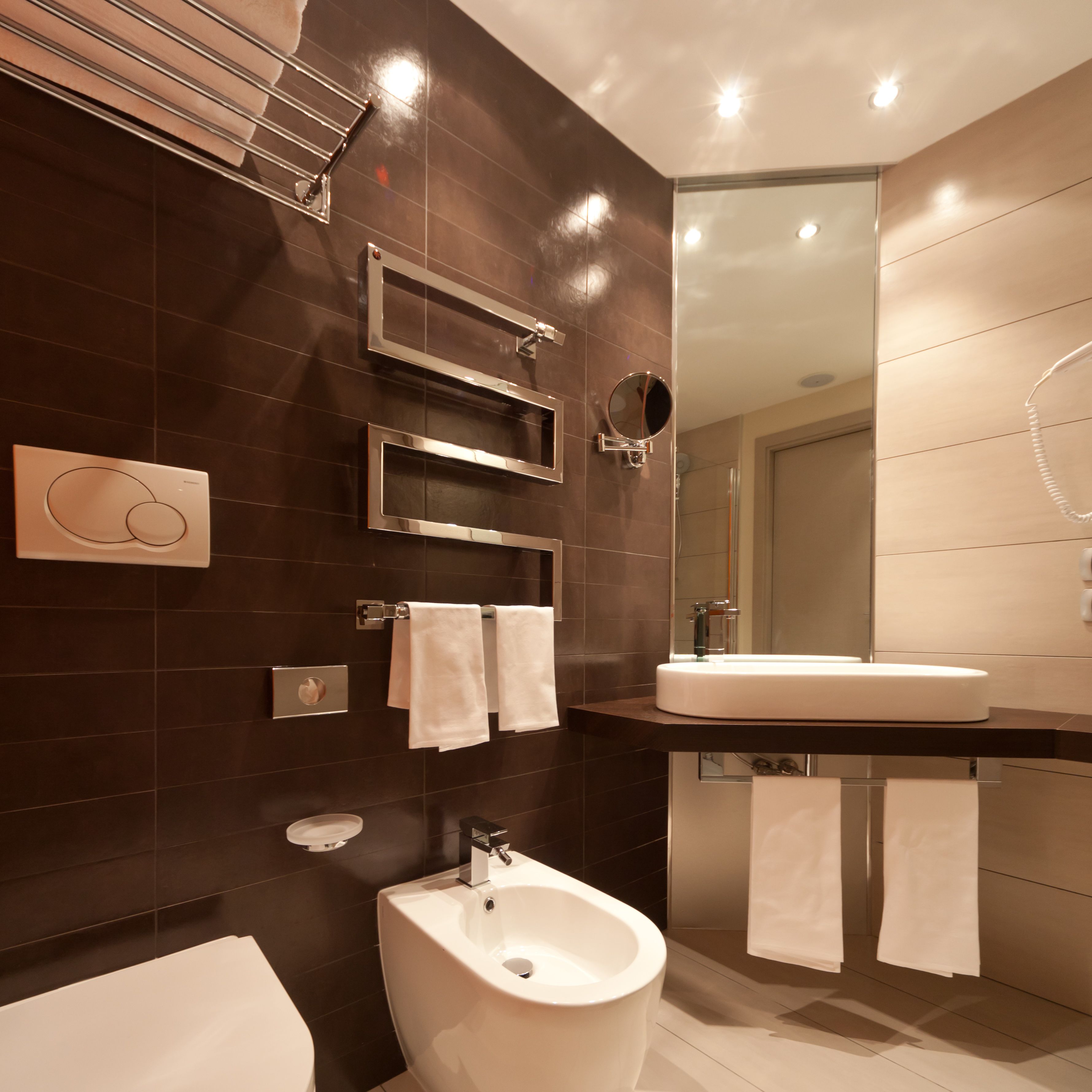 Un baño moderno con un bidé, un espejo grande y un lavamanos.