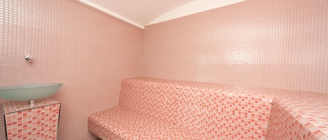 A bathroom with pink tiled walls, a glass sink, and a bench.