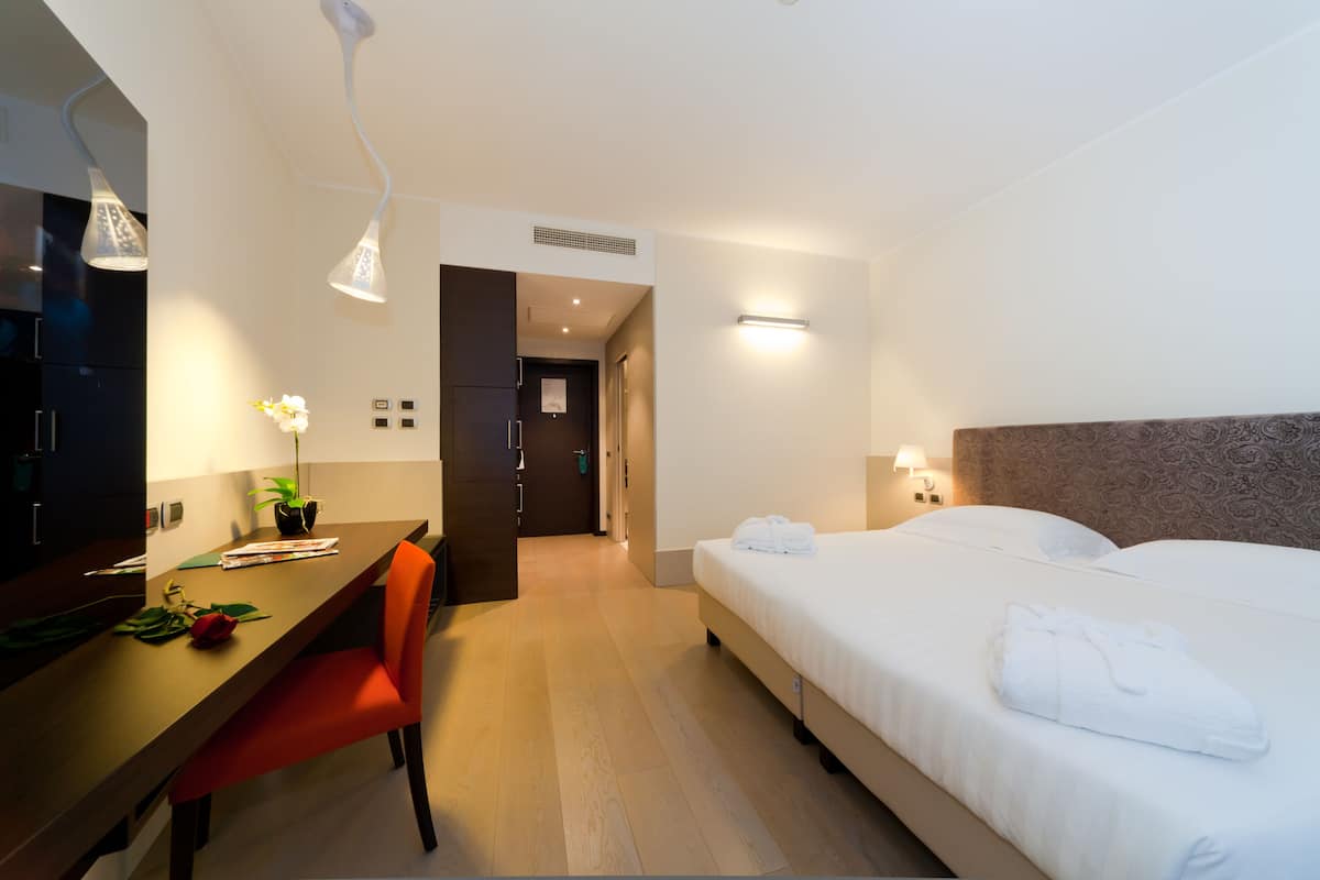Una habitación de hotel con cama, escritorio, silla, planta en maceta y espejo.