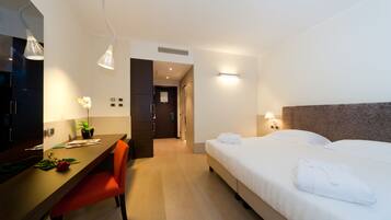 Une chambre d’hôtel avec un lit, un bureau, une chaise, une plante en pot et un miroir.