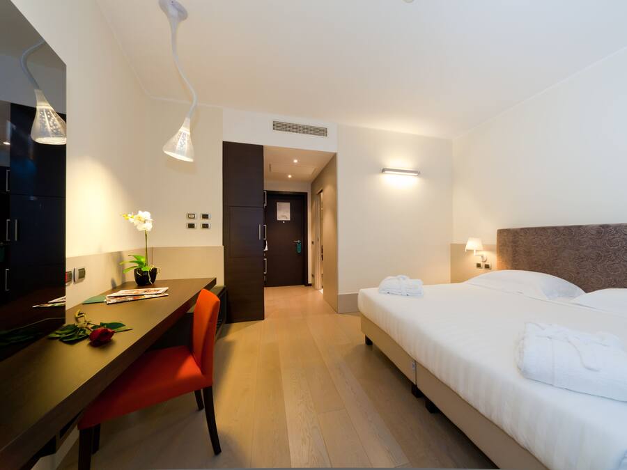 Una habitación de hotel con cama, escritorio, silla, planta en maceta y espejo.