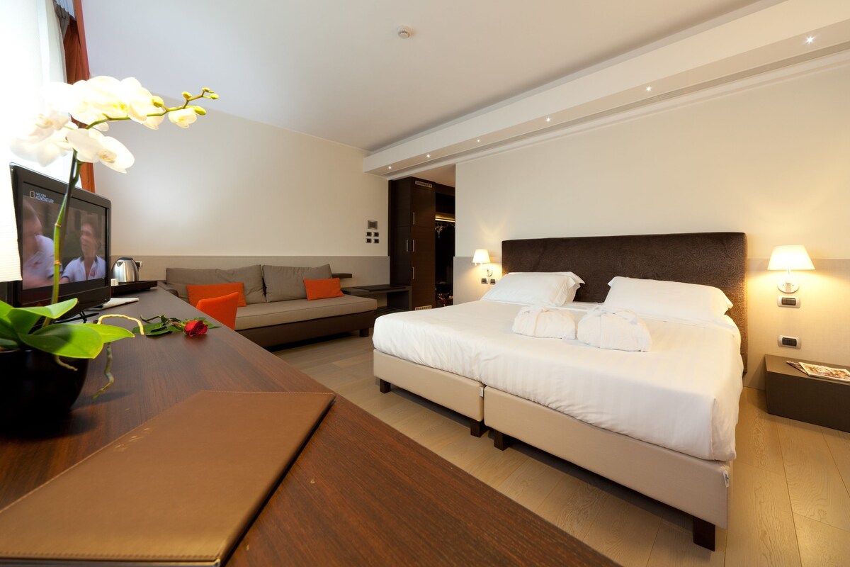 Una habitación de hotel con cama, un escritorio con una computadora portátil, un sofá y una televisión.