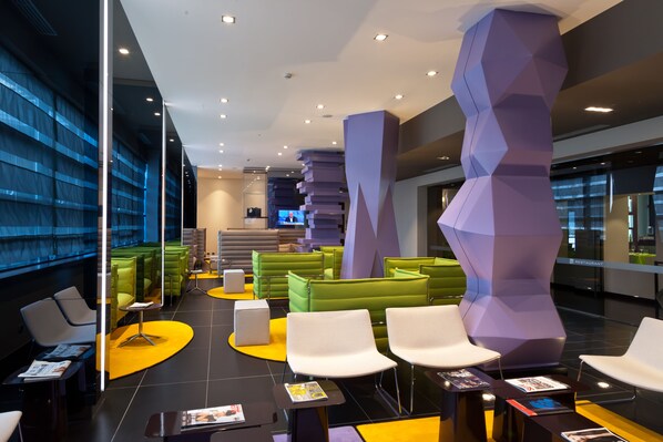 A modern lobby with green and white seating, a large purple column, and a digital screen in the background.