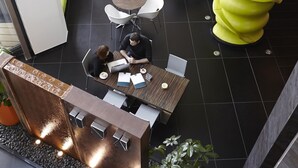 Un espacio interior moderno con un mostrador de recepción, zonas de estar y una escultura verde única.