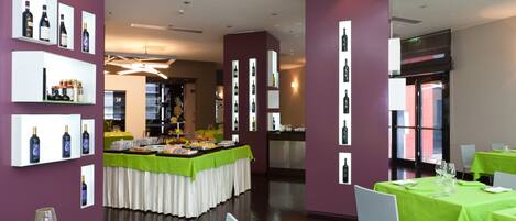 Un restaurante con una mesa de buffet central, rodeado de mesas con manteles verdes y sillas blancas.