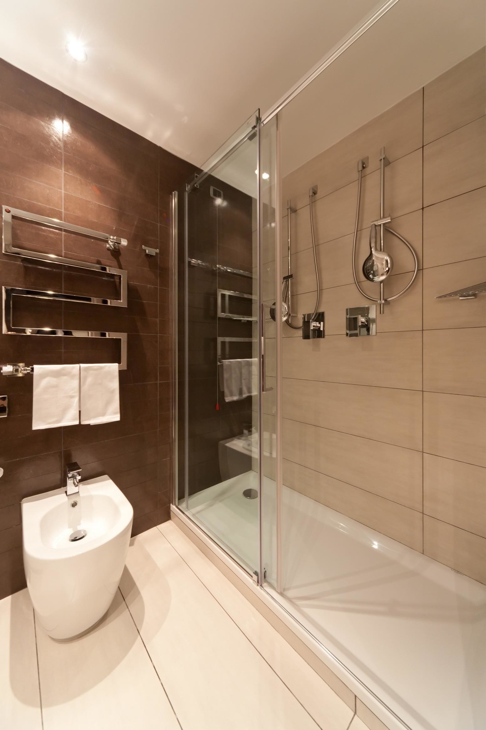 A modern bathroom with a bidet, a glass-enclosed shower, and a vanity with a mirror and towel rack.