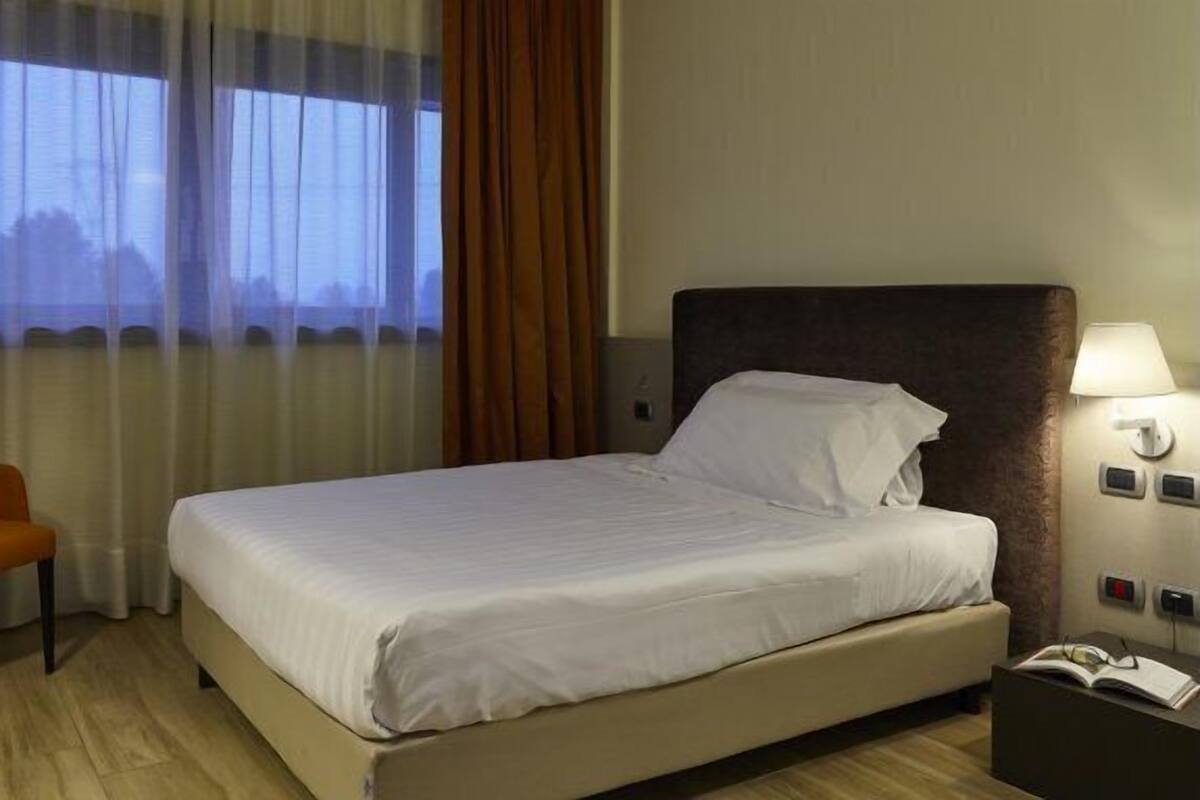 Una habitación de hotel con cama, una silla, una mesita de noche y una ventana con cortinas.