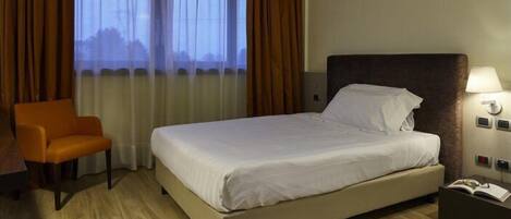 Una habitación de hotel con cama, una silla, una mesita de noche y una ventana con cortinas.