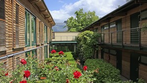 Un patio con edificios de madera, plantas verdes y flores rojas.