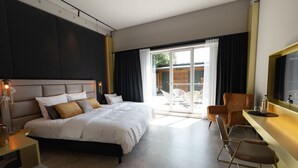 Habitación de hotel moderna con una cama grande, un escritorio y una silla. Hay una puerta corrediza de vidrio que da a un espacio exterior.