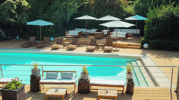 Un área junto a la piscina con sillones de descanso, sombrillas y una terraza de madera.