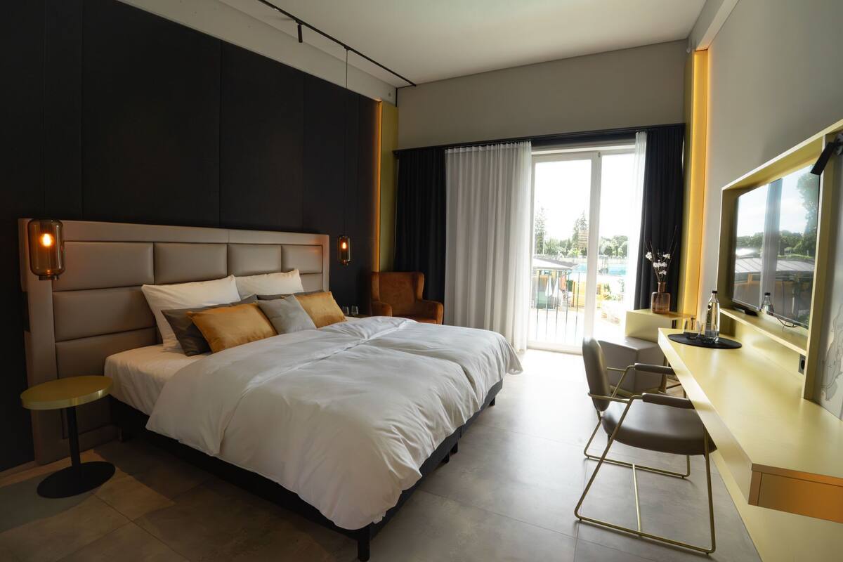 Una habitación de hotel moderna con una cama grande, un escritorio con una silla, televisión y un balcón con vistas.