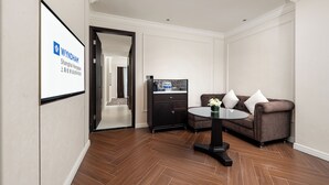 A modern hotel room with a wooden floor, a brown sofa, a small table, and a projection screen displaying the Wyndham logo. - Wyndham Shanghai Hongqiao (Shanghai)