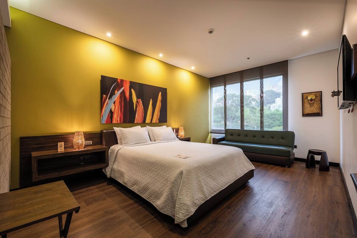 A modern bedroom with a large bed, a bench, a sofa, and a TV.
