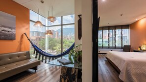 A modern hotel room with a hammock, a sofa, a bed, and large windows offering city views. - Diez Hotel Categoria Colombia (Medellín)