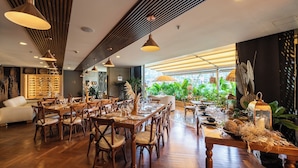 A restaurant with wooden tables and chairs, a wine rack, and a view of greenery through large windows. - Diez Hotel Categoria Colombia (Medellín)