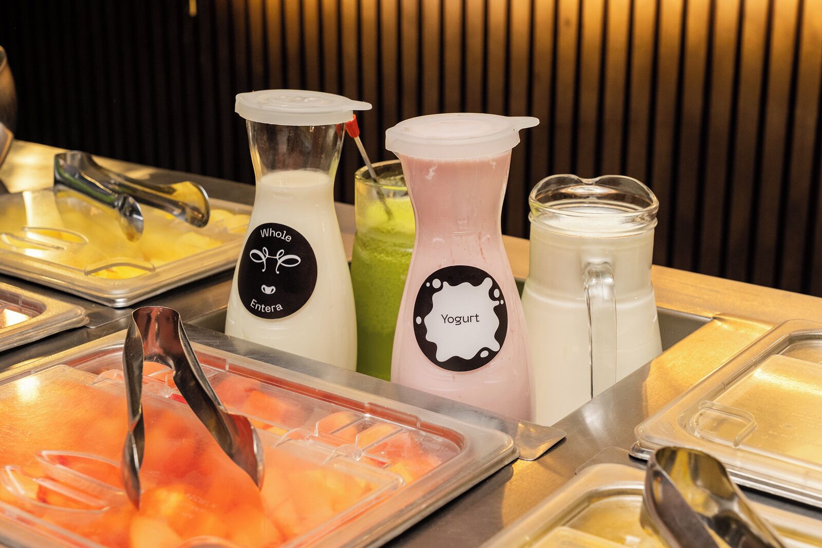 Un bufé con diversas opciones de comida y bebida, incluyendo un batido de yogur y un smoothie verde.