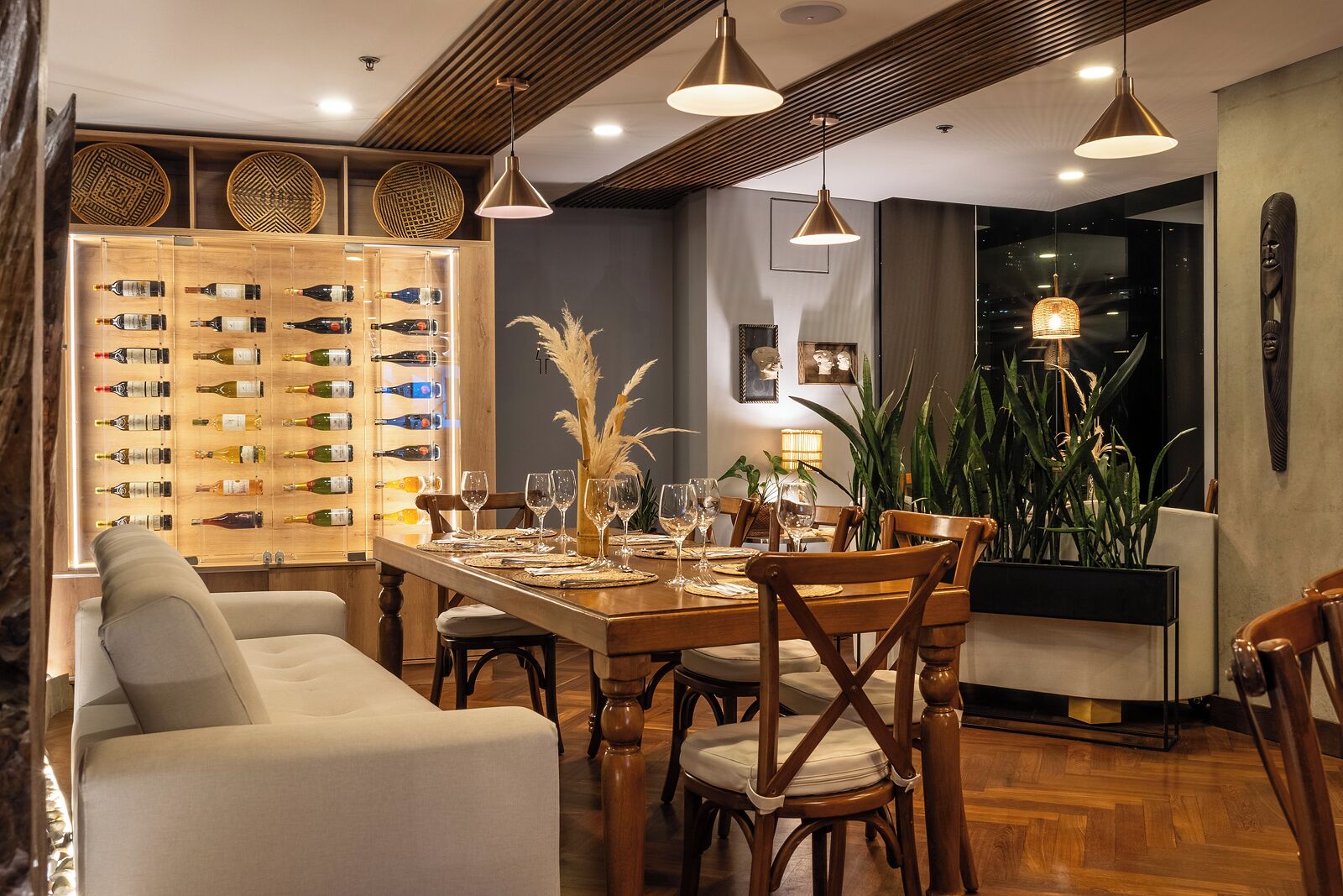 A dining area with a wooden table set for six, surrounded by upholstered chairs. A wine rack with bottles is visible to the left.