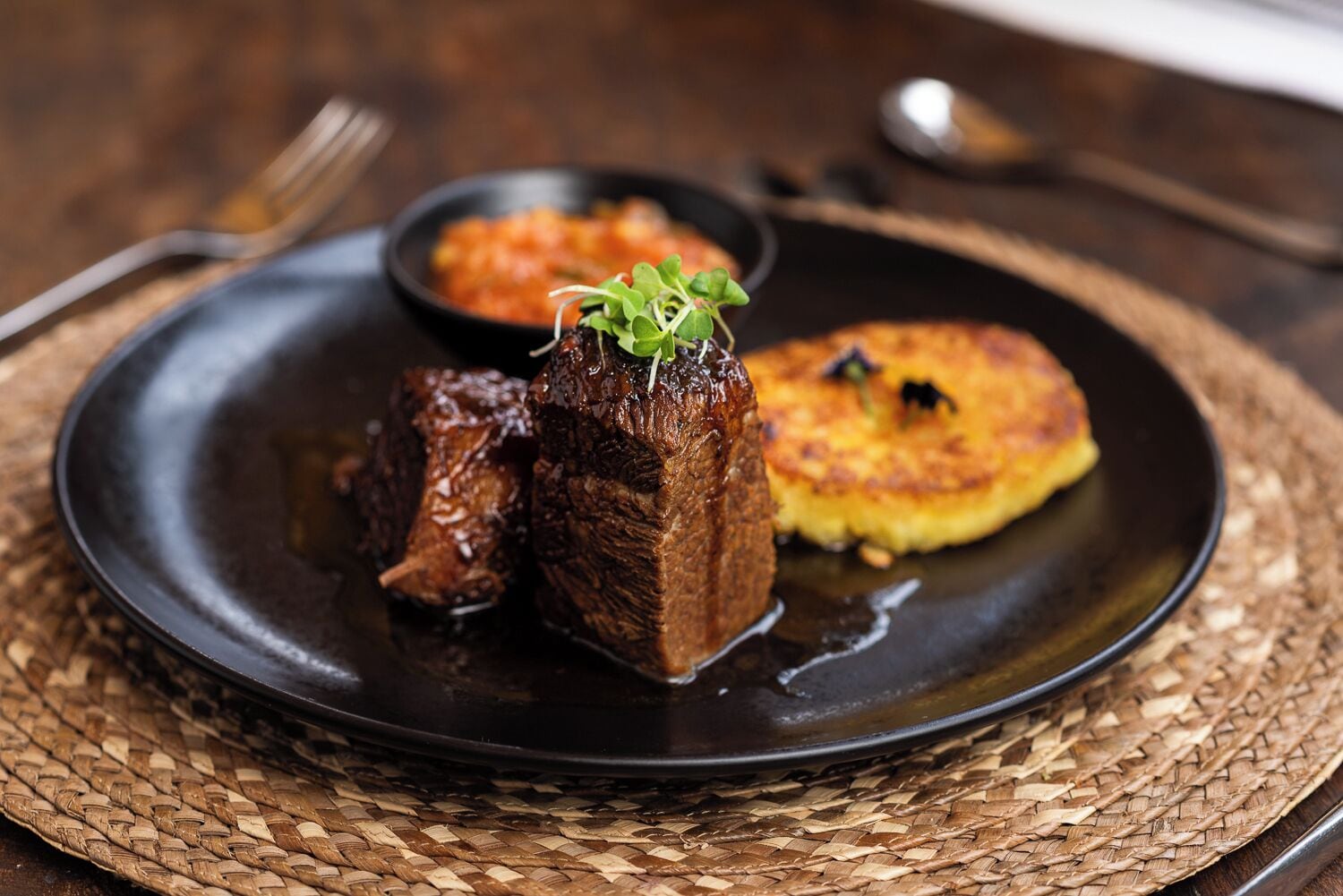 A plate with a piece of meat, a small bowl of sauce, and a potato dish.