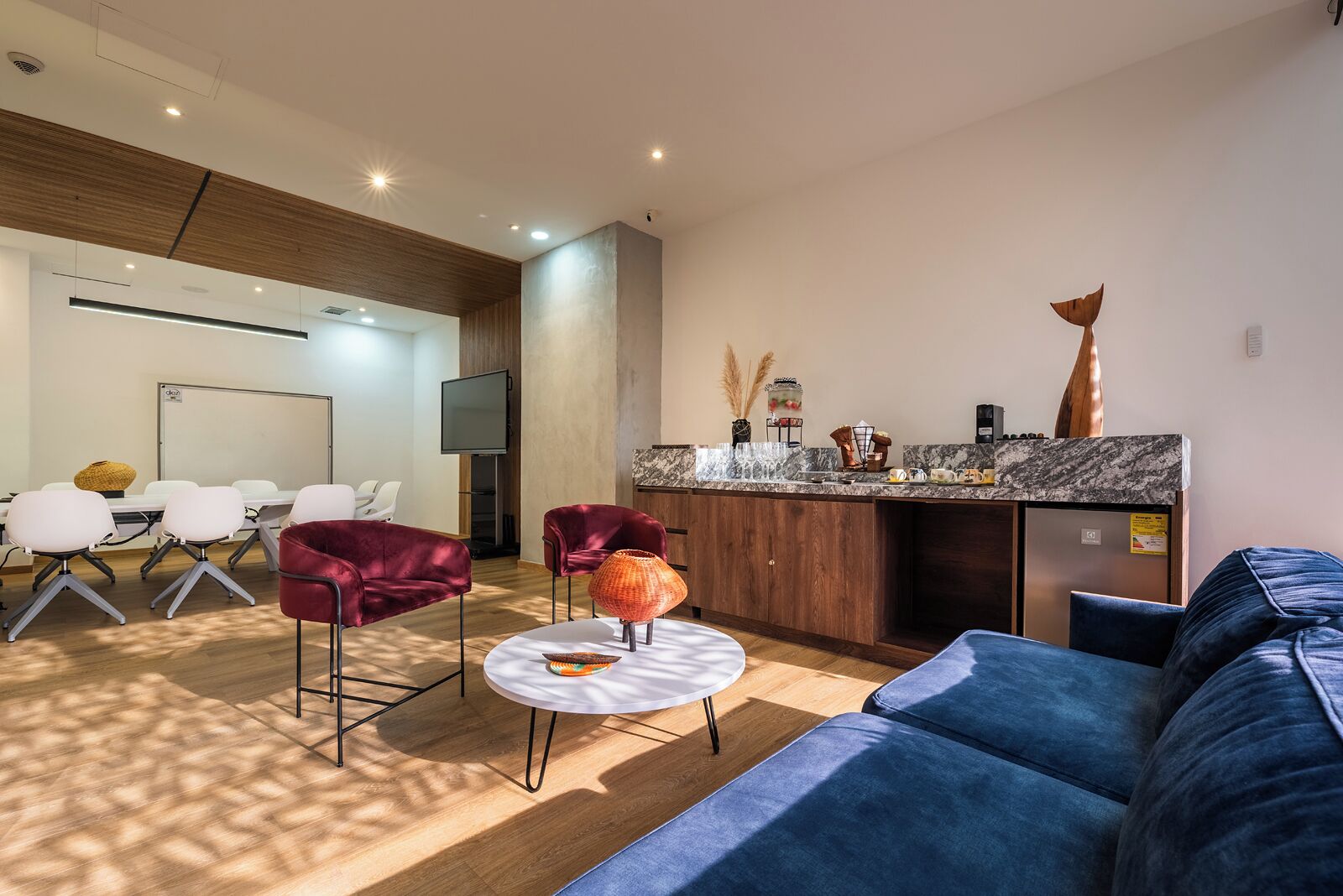 A modern hotel lobby with a seating area, a kitchen counter, and a television.