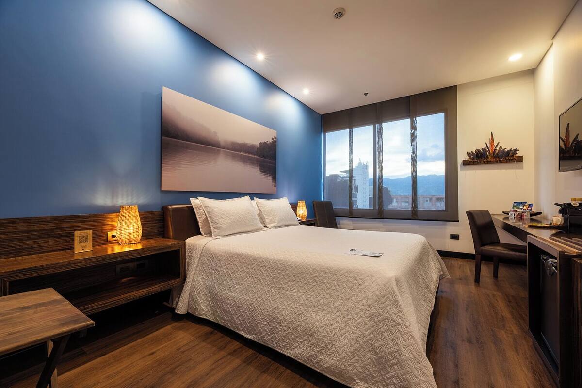A modern hotel room with a large bed, a desk, and a view of the city.