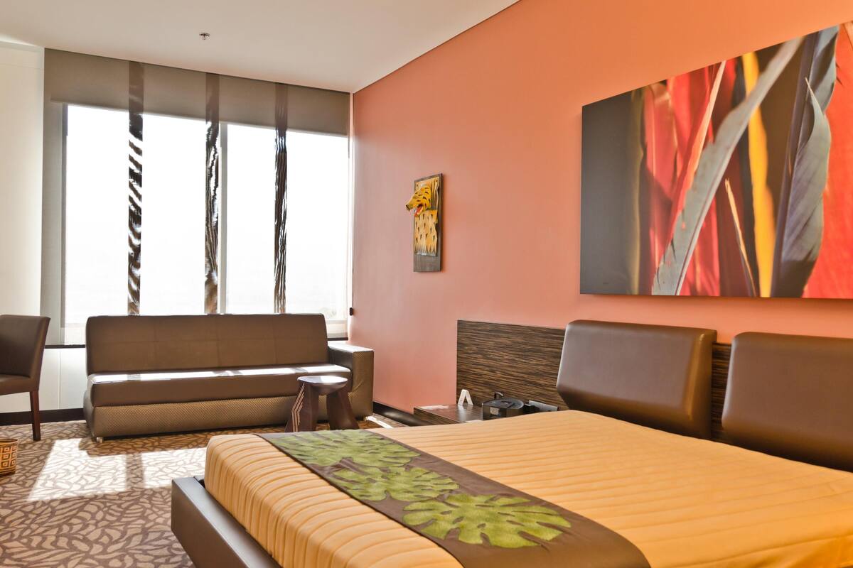 A hotel room with a bed, a sofa, a desk, and a large window with curtains.