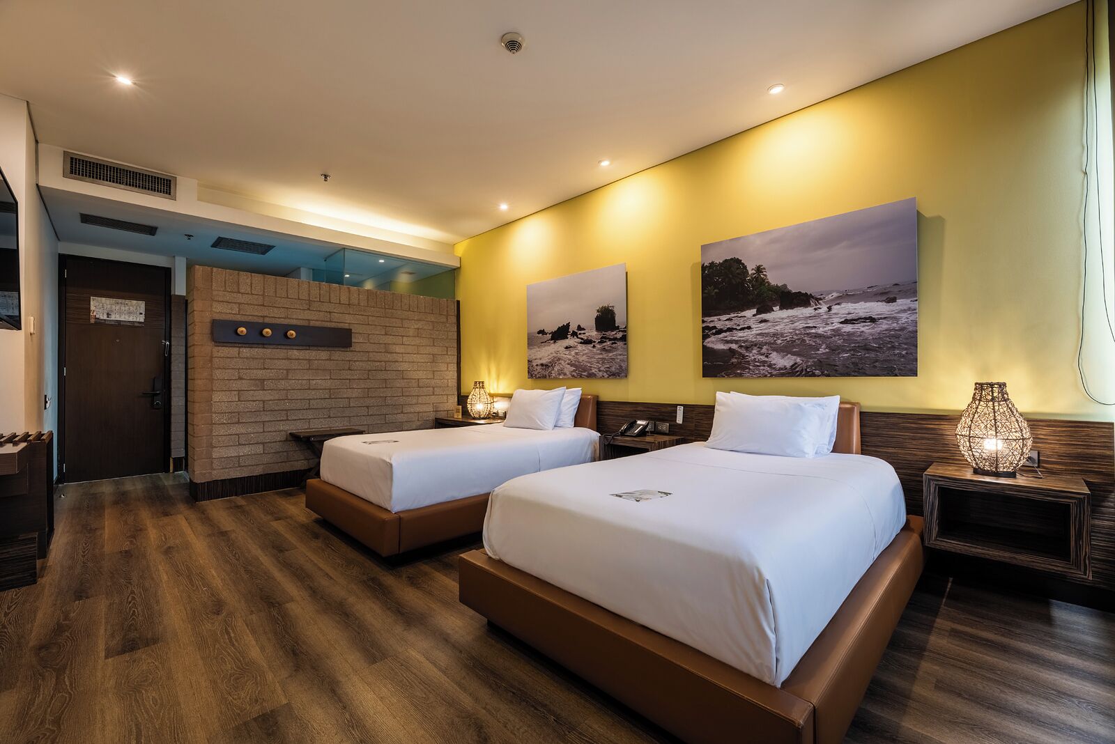 Habitación de hotel con dos camas, pared de ladrillo decorativa, obras de arte y suelo de madera.