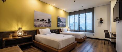 A hotel room with two beds, a desk, a chair, and a large window with a city view.