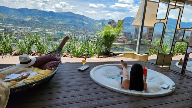 A person relaxing in a hot tub with a view of mountains and a cityscape. - Diez Hotel Categoria Colombia (Medellín)