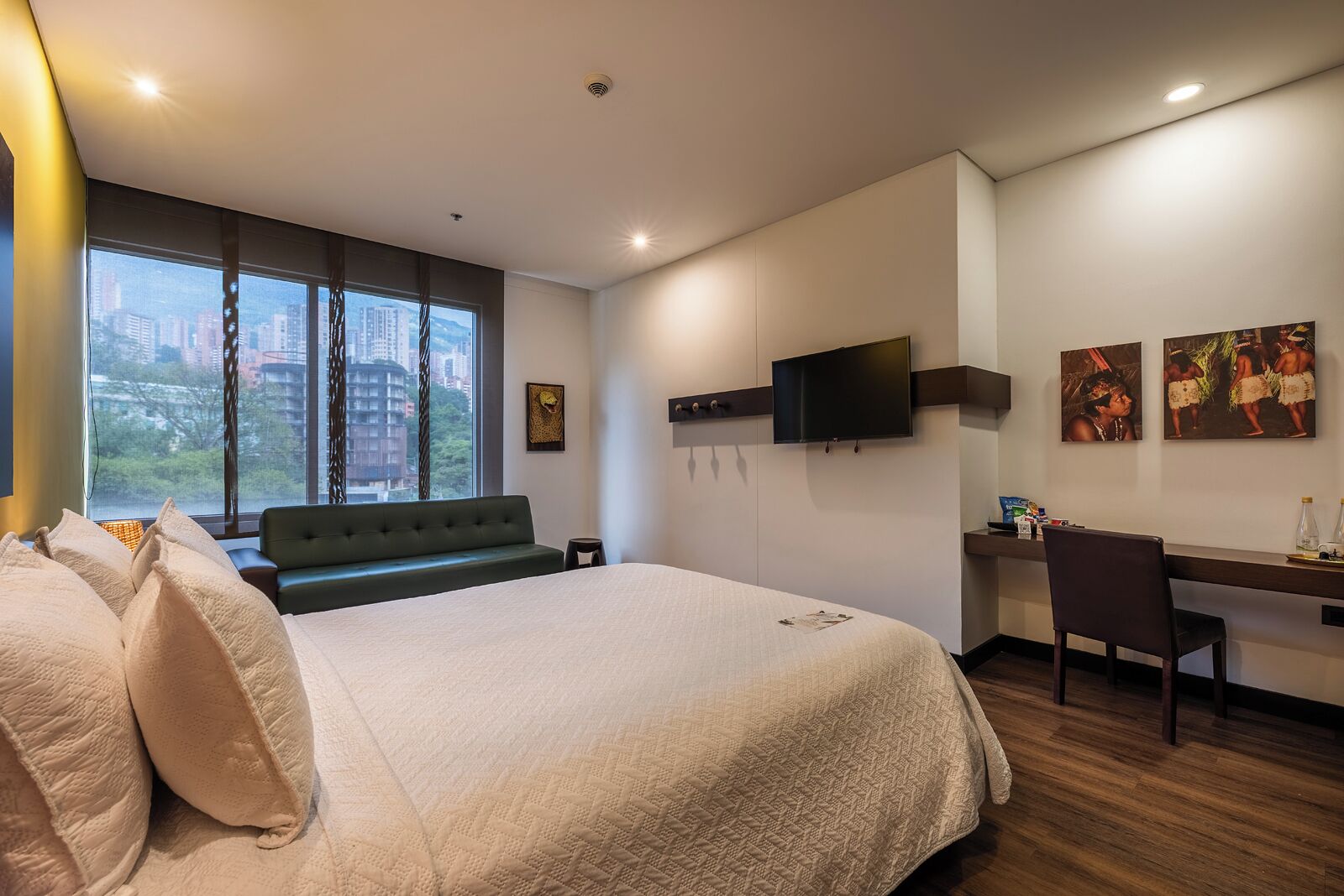 A hotel room with a large bed, a desk, a chair, a TV, and artwork on the walls.