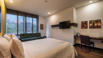 Una habitación de hotel con una cama grande, un escritorio, una silla, un televisor y obras de arte en las paredes.