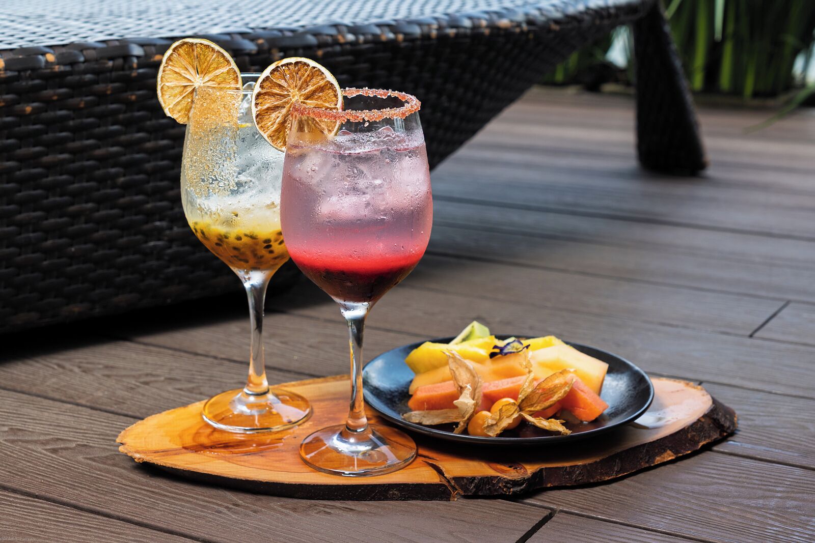 Two drinks on a wooden board with a plate of fruit.