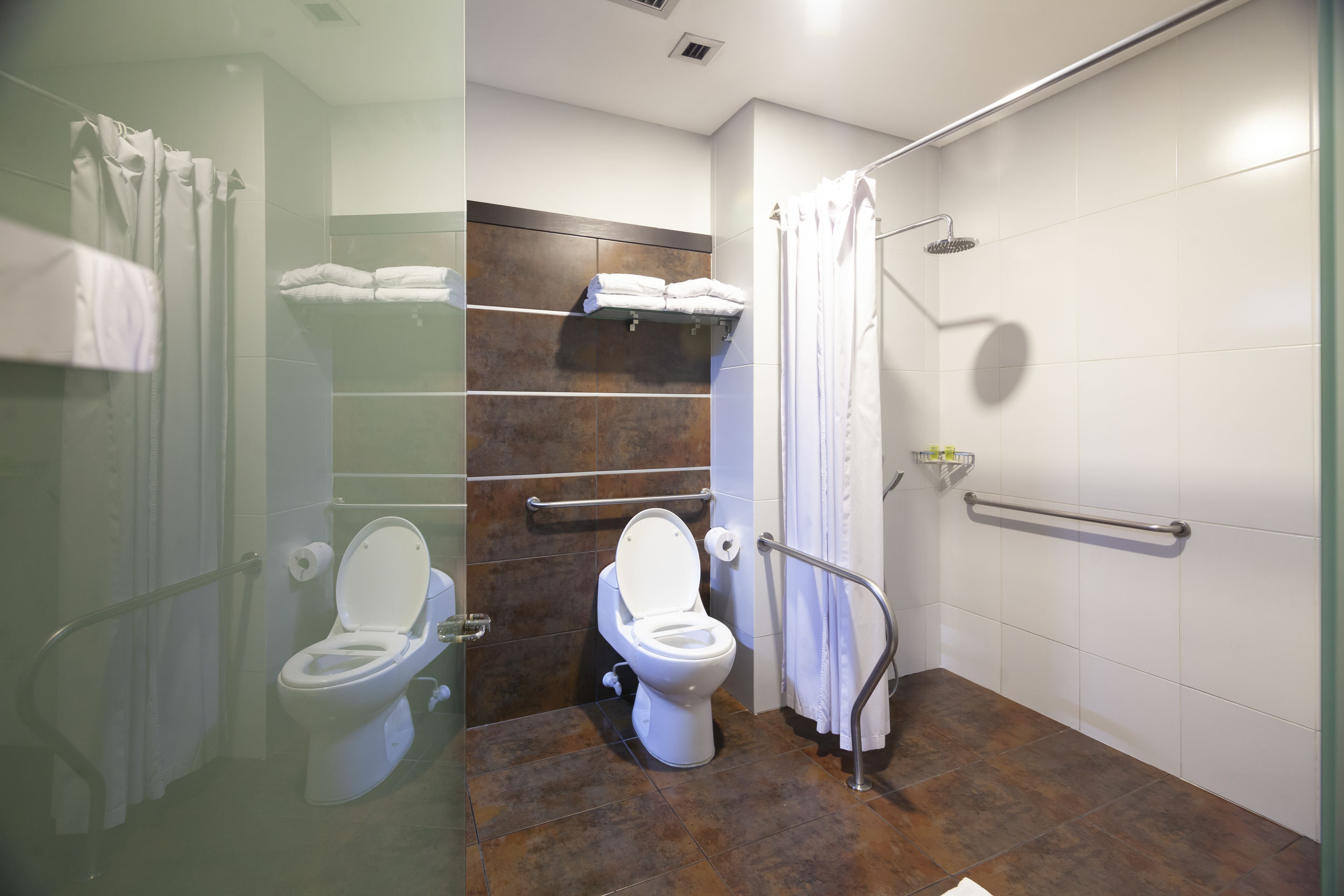 A bathroom with two toilets, a shower with a glass door, and a towel rack with folded towels.