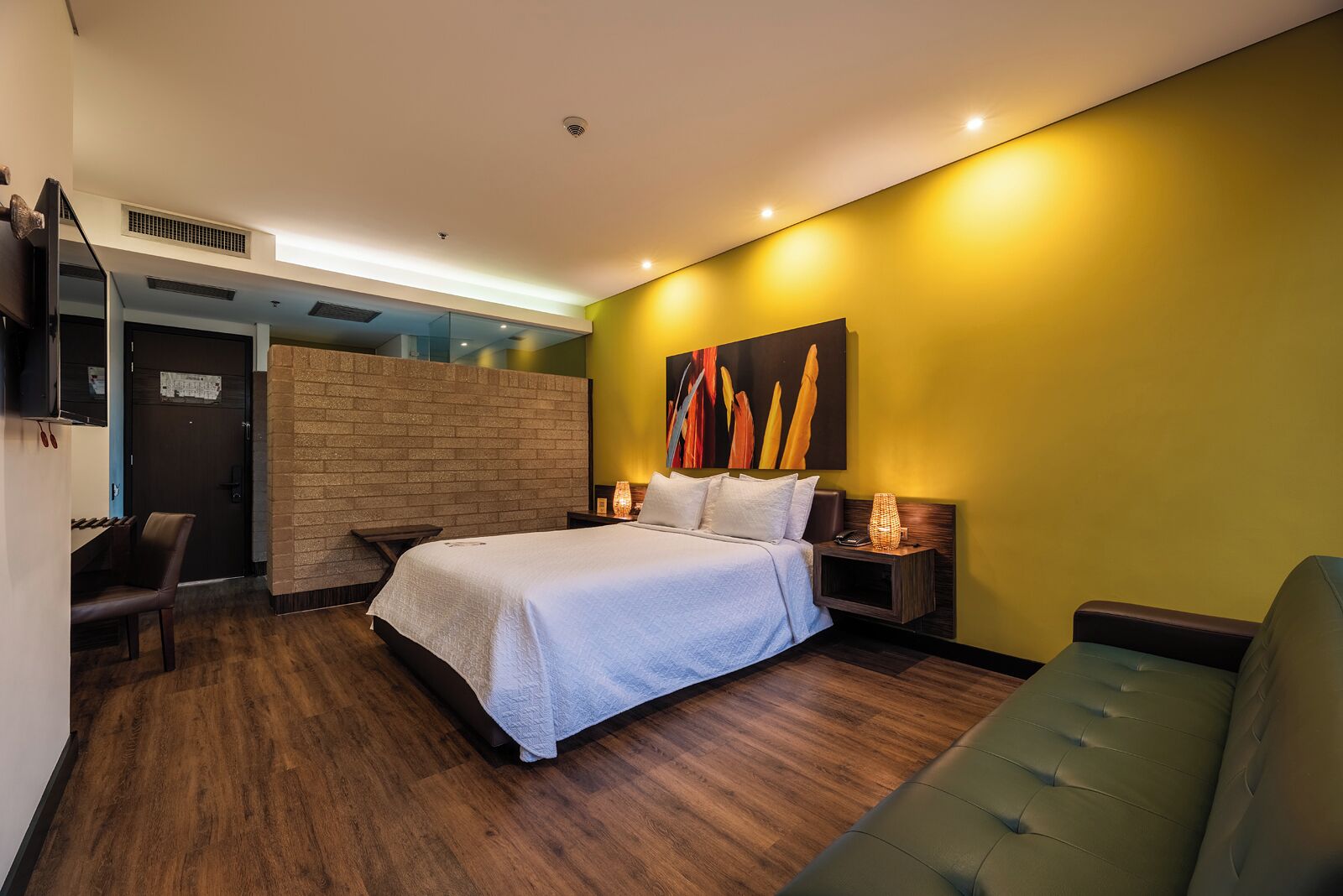 A modern hotel room with a bed, a seating area, a wall-mounted TV, and a painting.