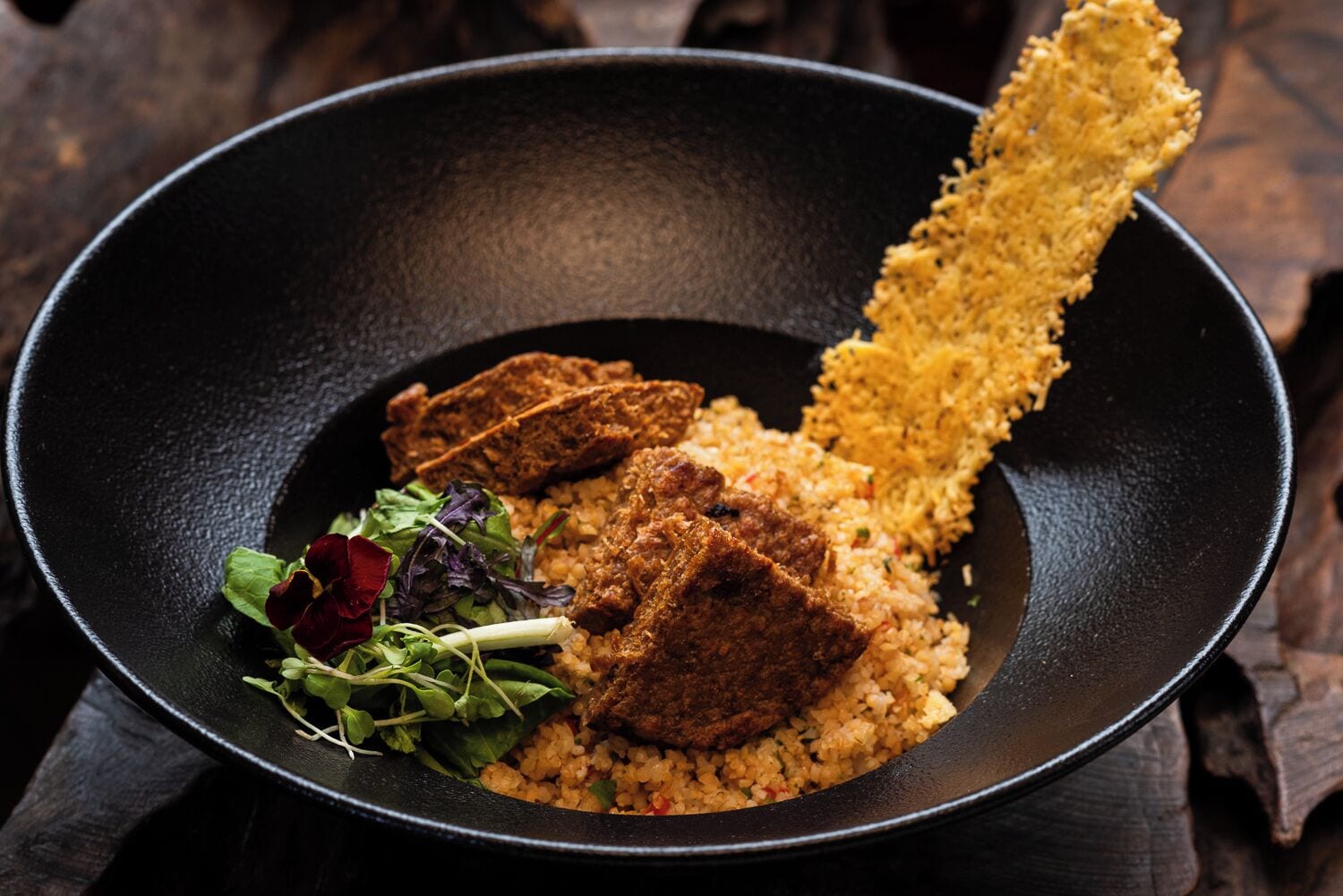 Un tazón negro con un plato de arroz, carne y algo frito, acompañado de una ensalada pequeña.