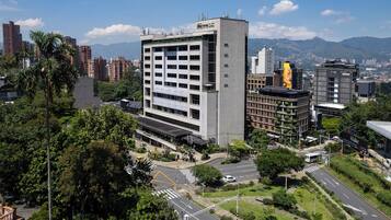 Un hotel de varios pisos con un diseño moderno, situado en una zona urbana rodeado de edificios y vegetación.